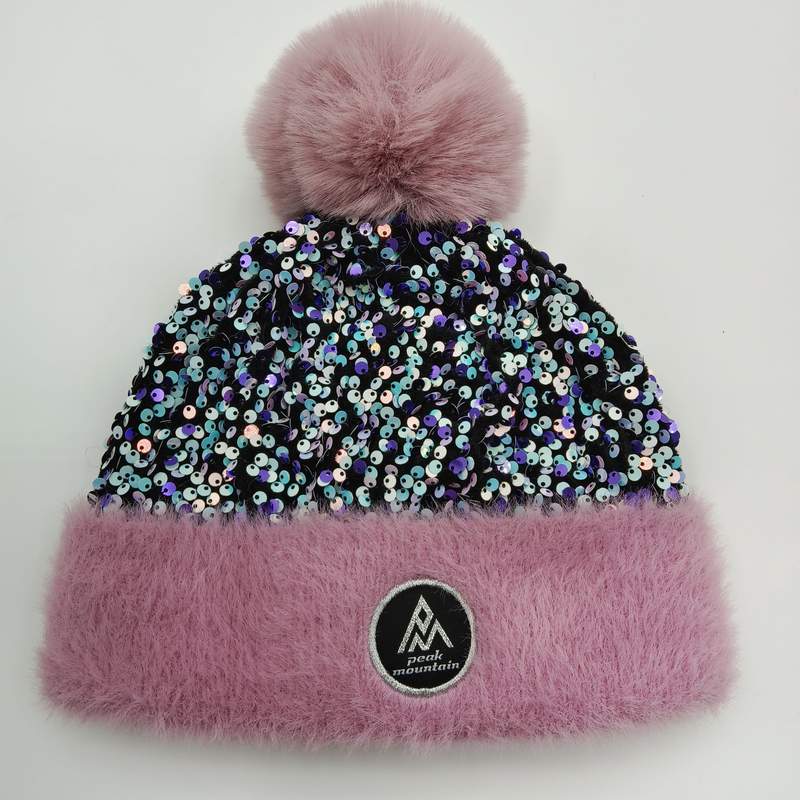 Rosafarbene Wintermütze mit schimmerndem Paillettenkörper, fluffigem Kunstpelz-Bündchen in Pink und großem Bommel auf weißem Hintergrund