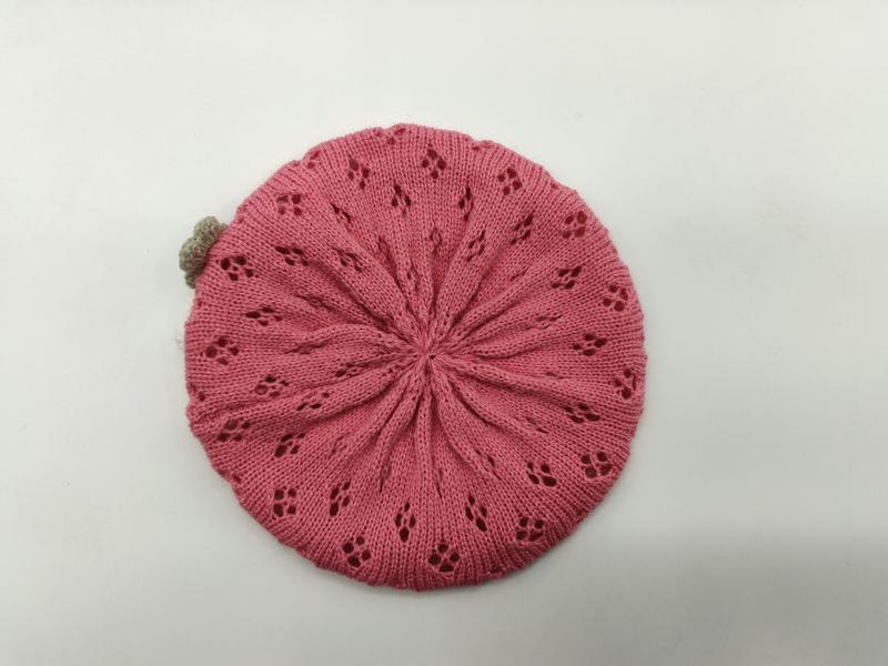 Draufsicht auf eine rosafarbene gestrickte Baskenmütze mit sternförmigen Lochstrickmustern und kleinem sandfarbenen Pompon auf weißem Grund