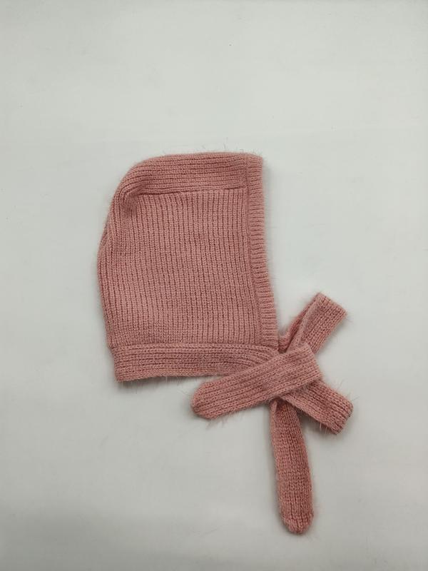 Weiche rosa Rippenstrick-Babyhaube mit langen Bindebändern, flach auf weißem Hintergrund