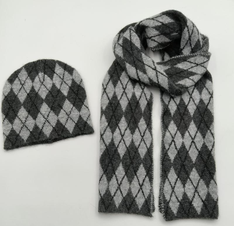 Aufeinander abgestimmtes Strickset aus Mütze und Schal mit Argyle-Rautenmuster in Anthrazit und Hellgrau, Draufsicht auf weißem Hintergrund