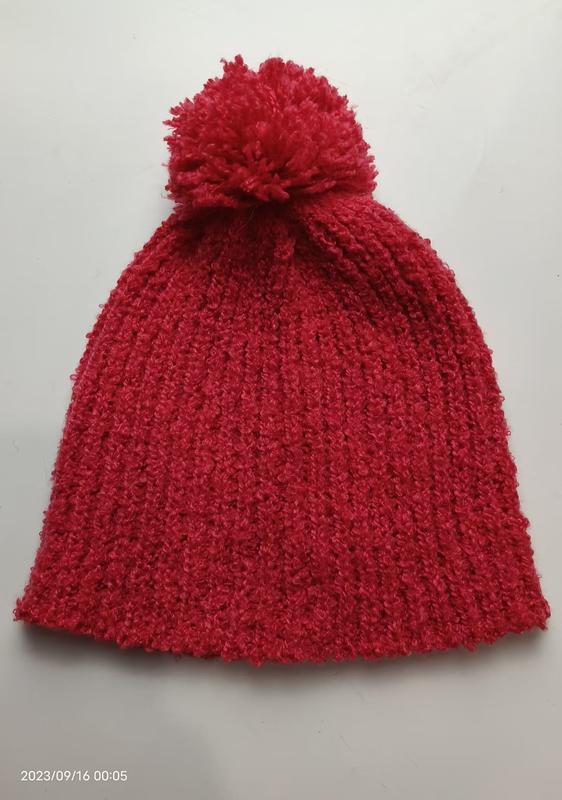 Rote strukturierte Rippenstrickmütze mit großem flauschigem Pompon auf der Spitze, flach auf weißem Hintergrund