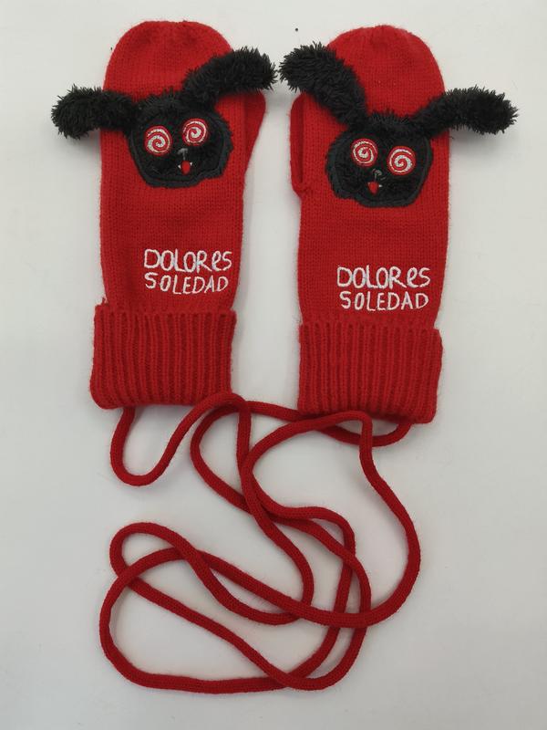 Rote gestrickte Handschuhe mit schwarzem Flausch-Monster-Motiv, Spiralaugen und langer Verbindungsschnur auf weißem Hintergrund