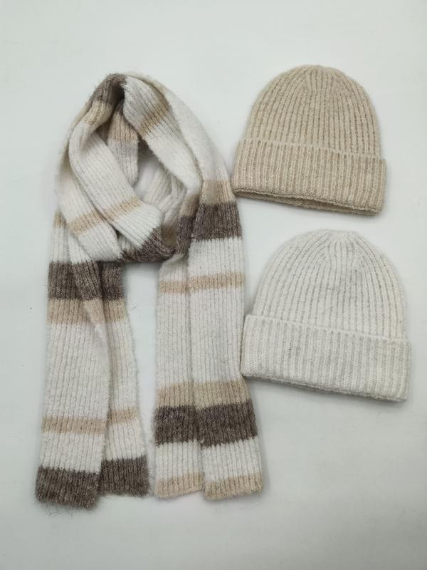 Zwei Rippenstrick-Beanies in Beige und Creme zusammen mit einem gemusterten Streifenstrickschal in Neutraltönen auf weißem Hintergrund