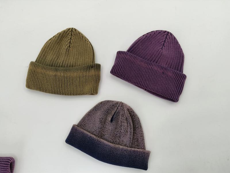 Drei zusammengelegte Rippstrickmützen in Olivgrün, gedämpftem Violett und zweifarbigem Grau-Dunkelblau nebeneinander