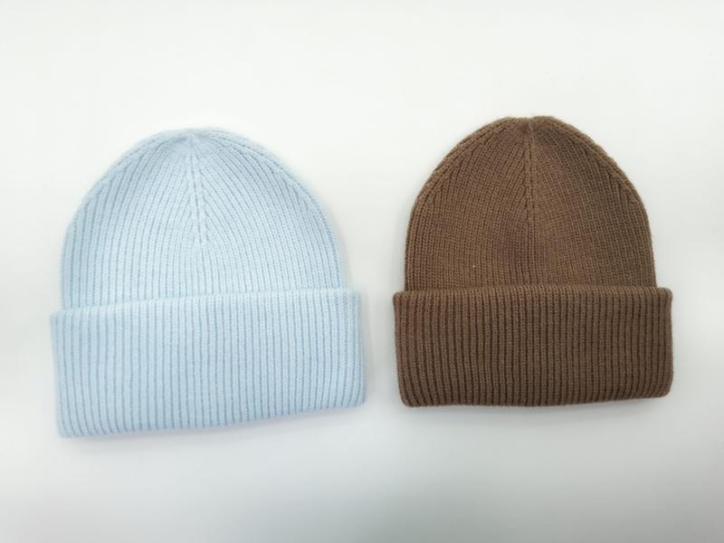Zwei gerippte Strickmützen nebeneinander, eine in Babyblau, eine in Karamellbraun, jeweils mit umgeschlagenem Bund auf weißem Hintergrund