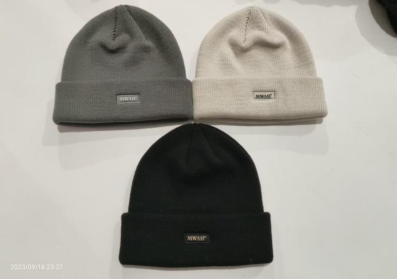Drei Rippenstrickmützen mit gefaltetem Bund in Anthrazit, Cremeweiß und Schwarz auf weißer Oberfläche mit Logo-Patch