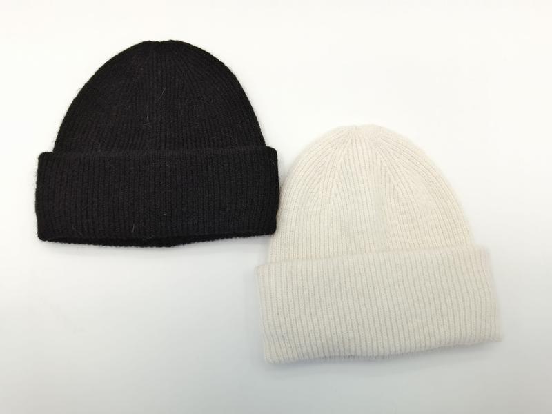 Zwei klassische Rippstrickmützen mit Umschlagrand nebeneinander – eine in Tiefschwarz, eine in gebrochenem Weiß, auf hellem Untergrund