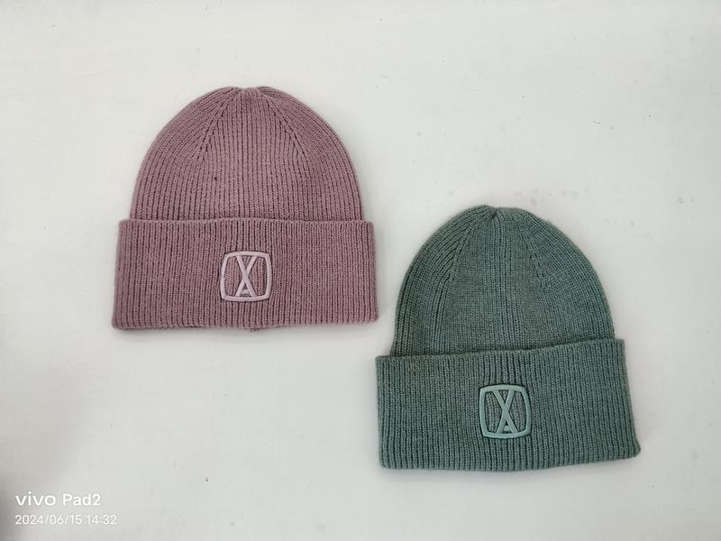 Zwei gefaltete Rippenstrickmützen in altrosa und salbeigrün mit dezenter Logostickerei, Draufsicht auf hellem Untergrund
