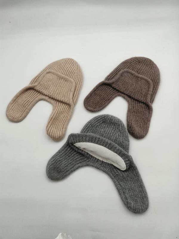 Drei Rippenstrick-Mützen mit seitlichen Ohrklappen in Beige, Braun und Grau nebeneinander auf weißem Hintergrund