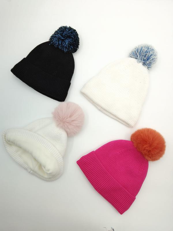 Vier Rippenstrickmützen mit bunten Bommeln in Schwarz, Weiß und Fuchsia-Pink, flach auf weißem Hintergrund angeordnet