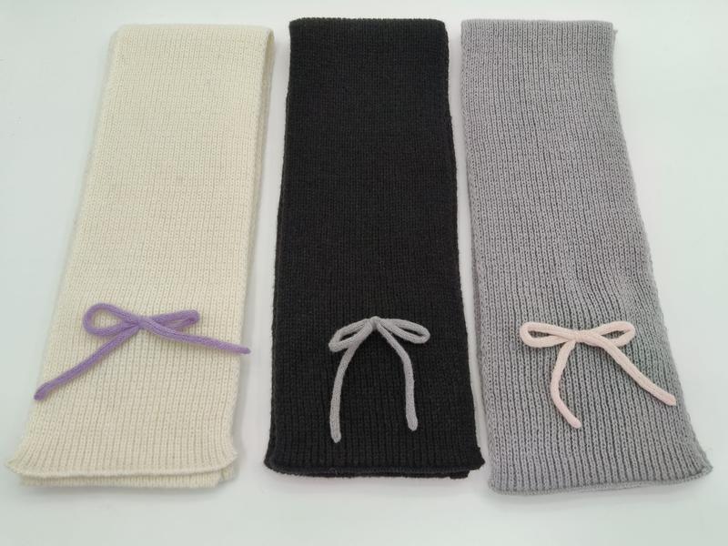 Drei elegante Strickschals in Creme, Anthrazit und Hellgrau mit dekorativer Garnschleife, glatt auf hellem Untergrund fotografiert