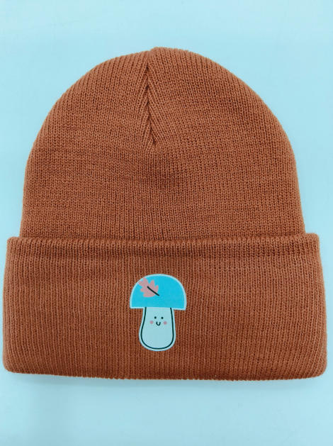 Rostbraune Rippenstrick-Umschlagmütze mit kawaii Pilzfigur als Aufnäher auf der Krempe, flach fotografiert