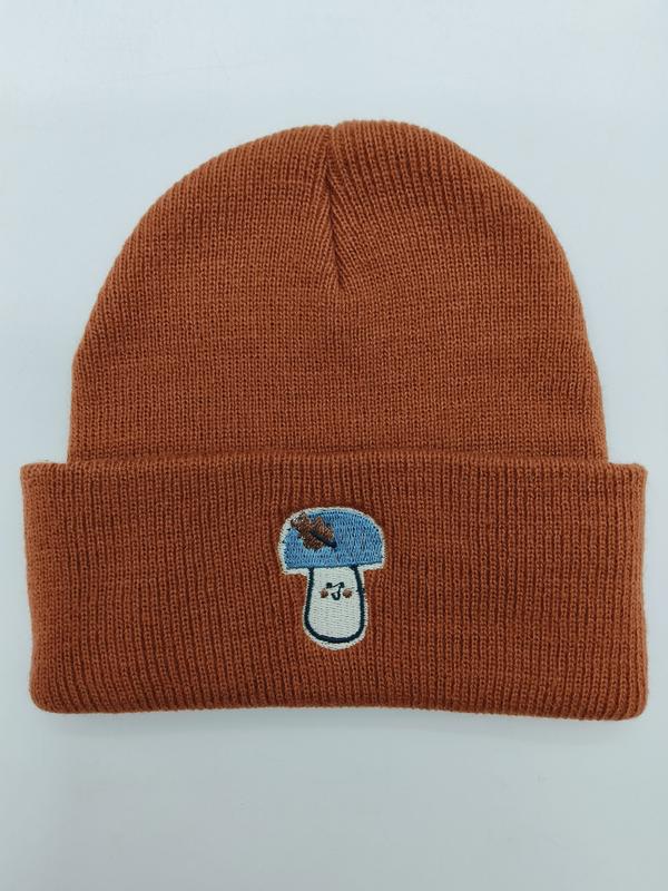 Rostfarbene Strickmütze mit breitem Umschlag und farbenfrohem Pilz-Stickerei-Aufnäher in Blau und Weiß auf der Krempe