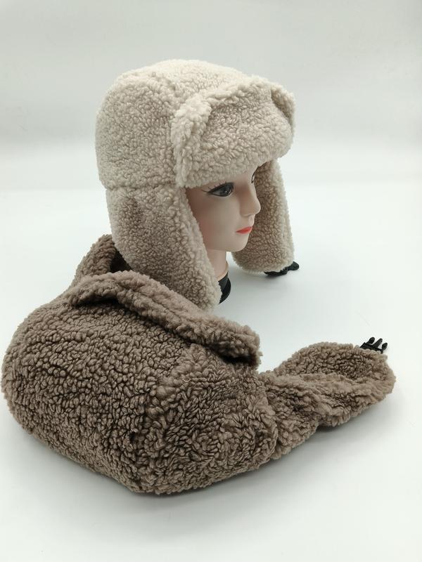 Zweifarbige Sherpa-Mütze in Creme und Beige mit weichem Fleece-Material und herunterklappbaren Ohrenschützern auf Hutständer