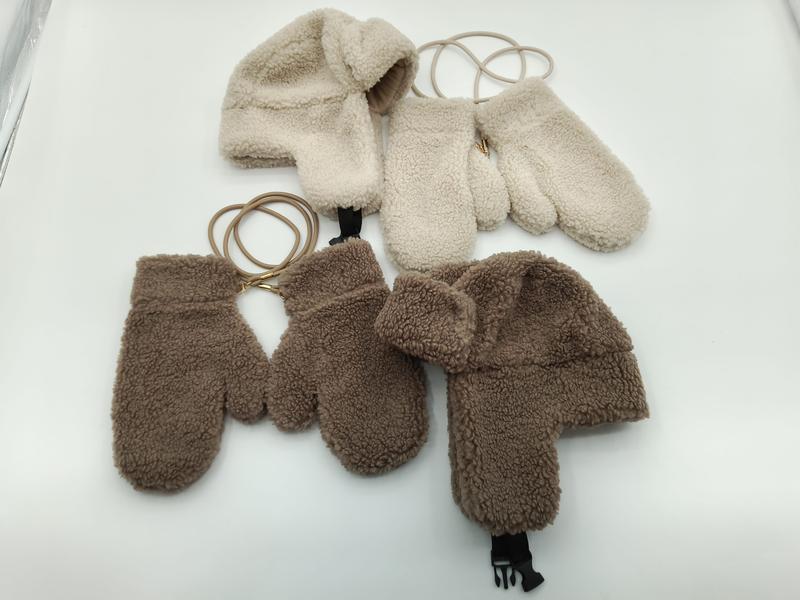 Zwei kuschelige Sherpa-Fleece-Trappermützen mit passenden Fäustlingen in Creme und Braun, durch elastische Halteschnur verbunden, flach auf weißem Hintergrund