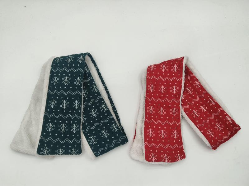 Zwei gefaltete Schals mit weißem Schneeflocken-Fair-Isle-Muster in Petrol und Rot mit sichtbarem Sherpa-Fleecefutter auf weißem Hintergrund