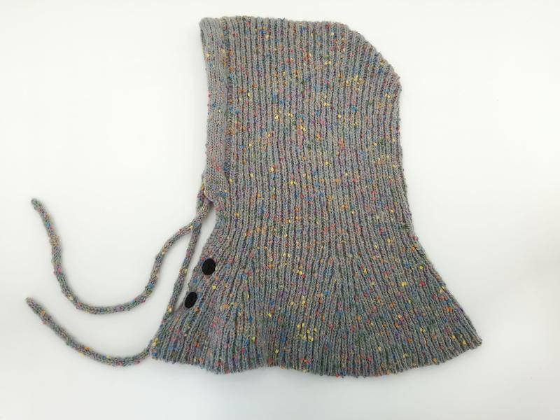 Graue mehrfarbig melierte Strick-Babyhaube mit Kinnbändern und zwei schwarzen Druckknöpfen, als Flachbild auf weißem Hintergrund