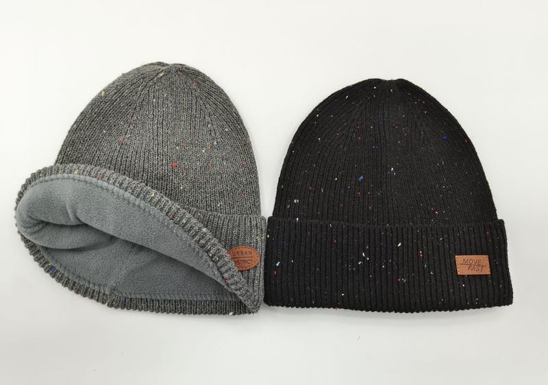 Zwei melierte Strickmützen nebeneinander: graue fleecegefütterte Rollmütze und schwarze Rippenmütze mit Umschlag und Leder-Patch