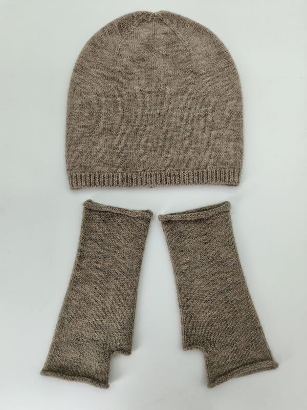 Meliertes Taupe-Beanie und passende fingerlose Strickhandschuhe flach auf weißem Untergrund arrangiert