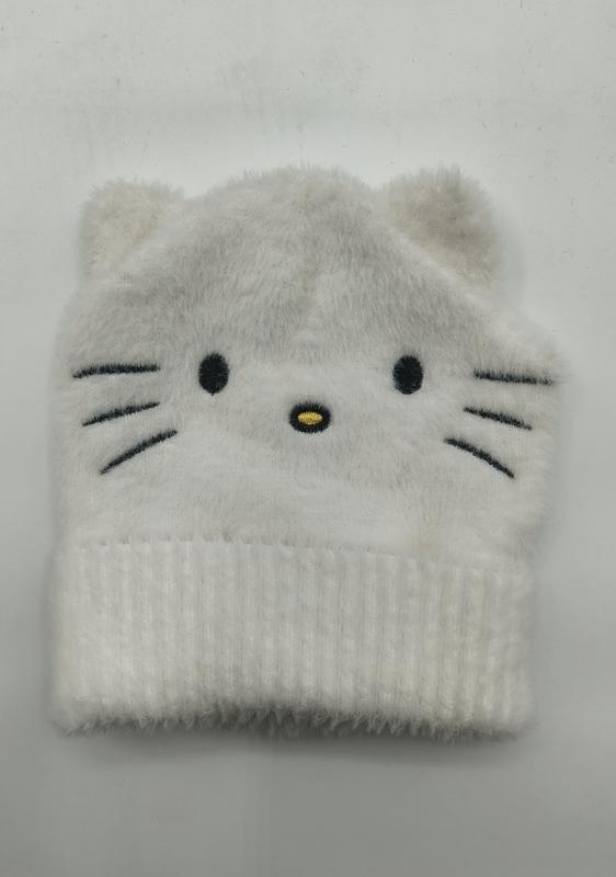 Weiße flauschige Strickmütze mit aufgesticktem Katzengesicht, Schnurrhärchen und kleinen spitzen Ohren, flach auf weißem Untergrund fotografiert